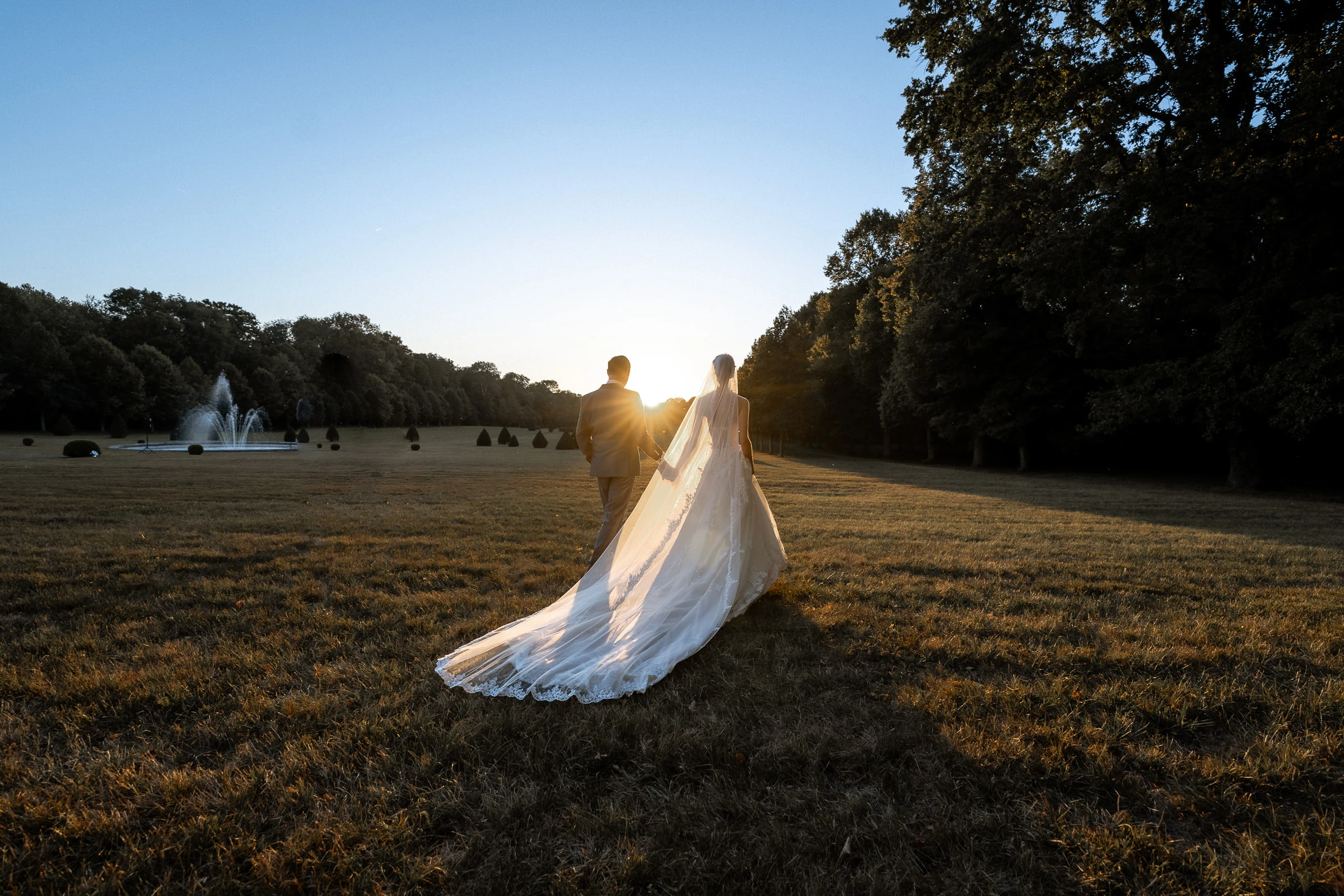 Les mariés s’éloignent au crépuscule dans le parc, voile déployé, château de Champlâtreux